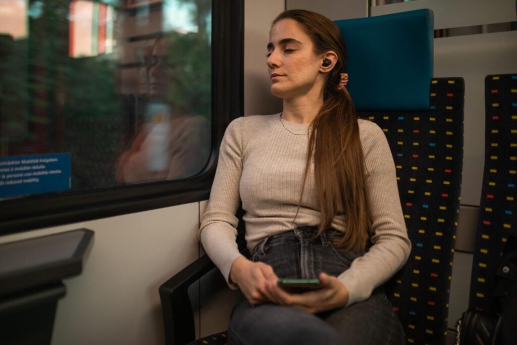 Tired female traveler casually sleeping in train while listening music on earbuds